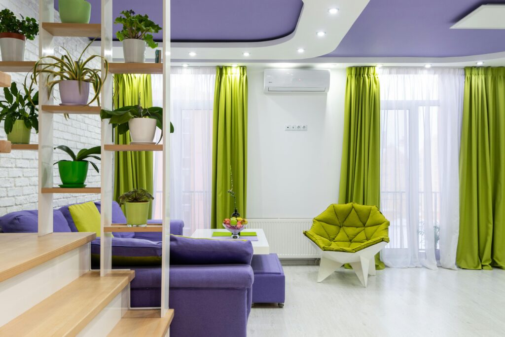 Interior of modern living room with bright purple sofa and ceiling and green armchair and curtains decorated with potted plants placed on creative shelves